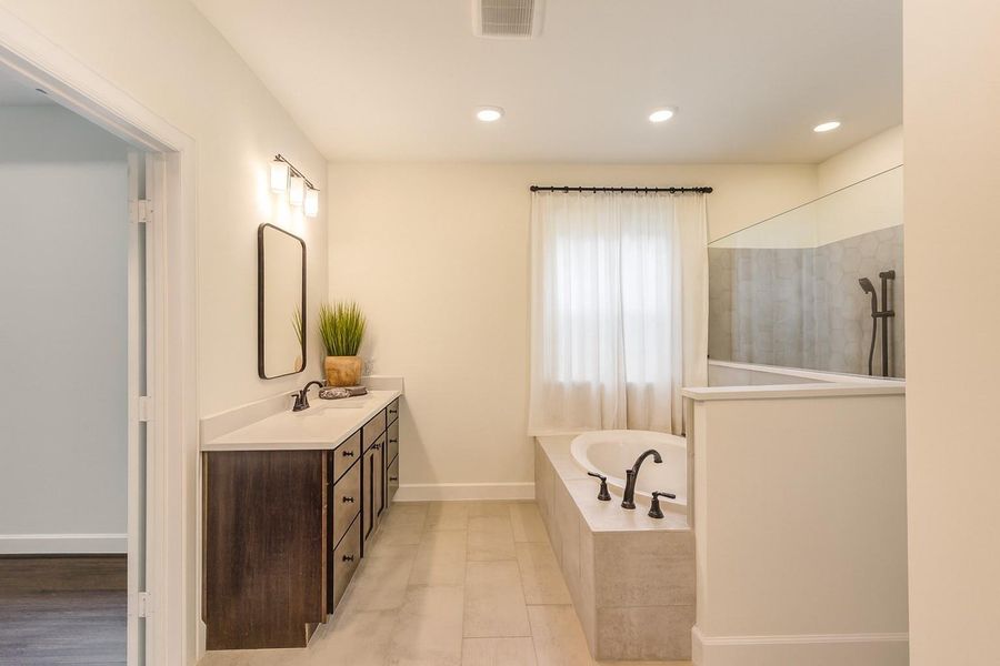This bathroom features a modern design with a double vanity, dark cabinetry, and sleek fixtures. It includes a spacious tub and separate shower, complemented by neutral tones and ample lighting.