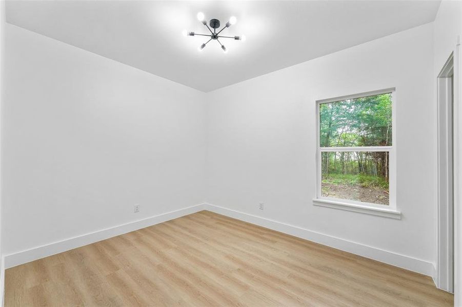 Open room featuring light wood-finish flooring, crisp white walls, and a contemporary black sputnik-style ceiling light Open room featuring light wood-finish flooring, crisp white walls, and a contemporary black sputnik-style ceiling light