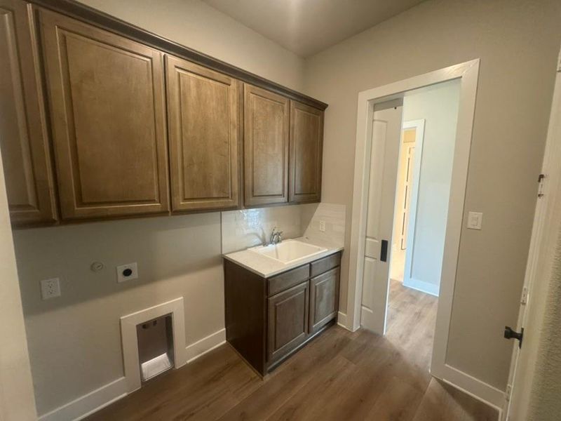 Laundry area featuring upper cabinetry, a utility sink with a quartz-finish countertop, and wood-finish flooring