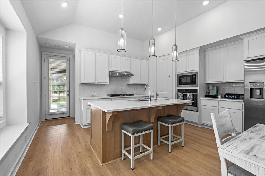 Kitchen features a spacious island with seating, complemented by wood flooring and an abundance of natural light. Kitchen features a spacious island with seating, complemented by wood flooring and an abundance of natural light.
