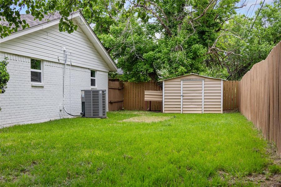 View of yard featuring a storage shed, a fenced backyard, central AC, and an outdoor structure View of yard featuring a storage shed, a fenced backyard, central AC, and an outdoor structure
