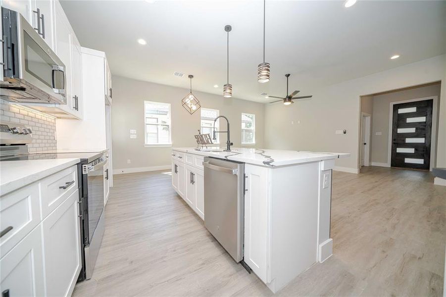 Kitchen featuring stainless steel appliances, white cabinetry, tasteful backsplash, ceiling fan, and light stone counters Kitchen featuring stainless steel appliances, white cabinetry, tasteful backsplash, ceiling fan, and light stone counters