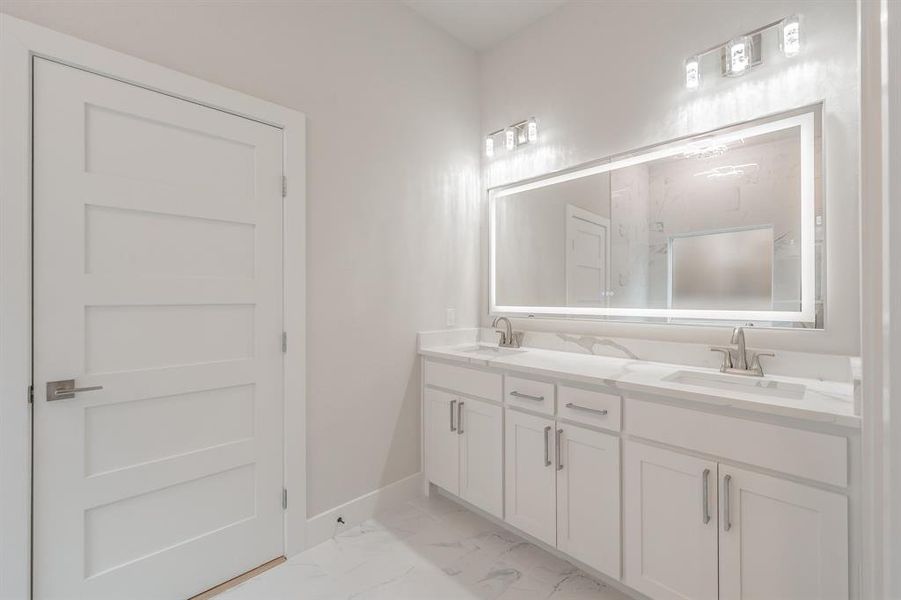 Full bath with double vanity, light marble finish floors, and a marble finish shower