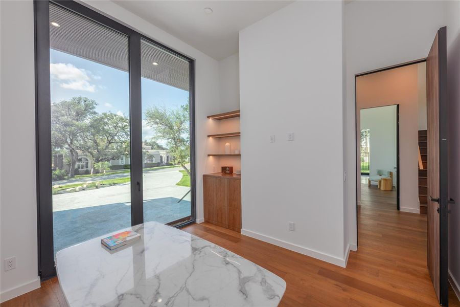 Panoramic windows flood this office with abundant natural light, highlighting the sleek hardwood floors and custom built-in shelving.