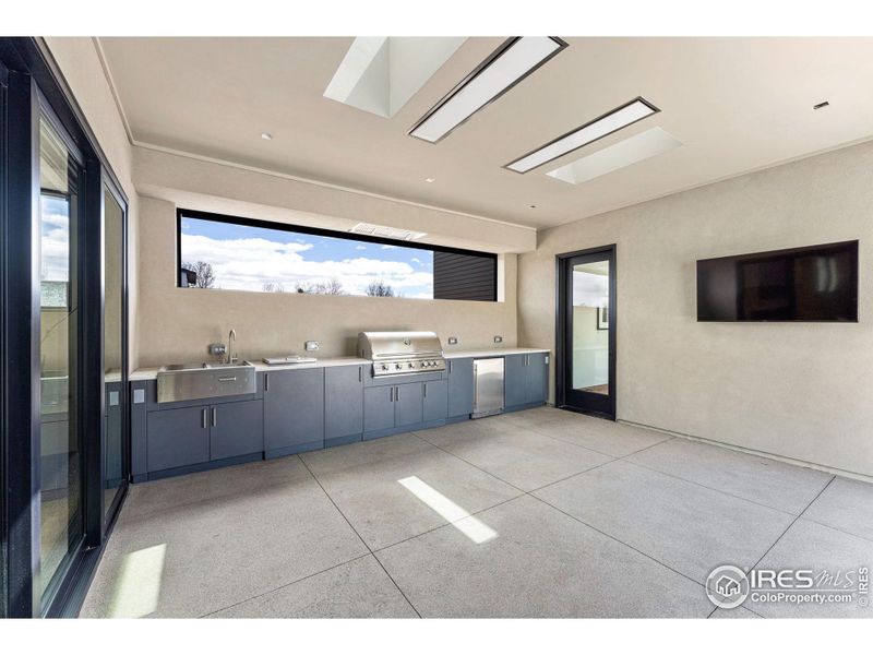 Outdoor Bonfire kitchen with metal cabinets, grill, refrigerator, sink, ice chest & Taj Mahal leathered quartz counters. Ceiling heaters, motorized screens & flatscreen wall mounted TV. Connecting the family room, pool house & outdoor pool, spa, & patio.