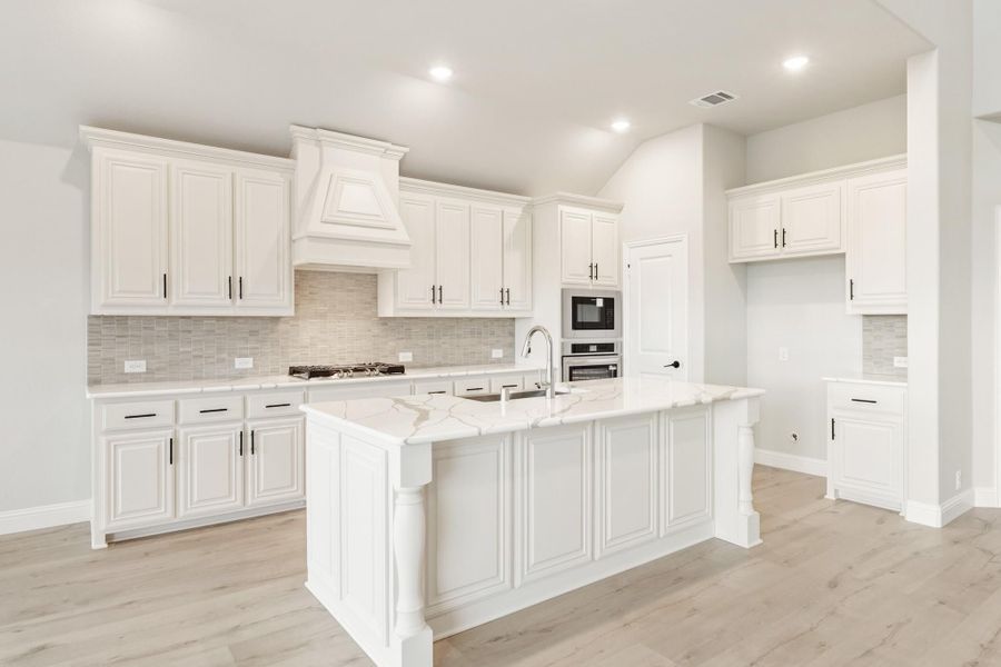 White kitchen with raised-panel cabinets, large center island, tile backsplash, and stainless steel appliances on light wood floors