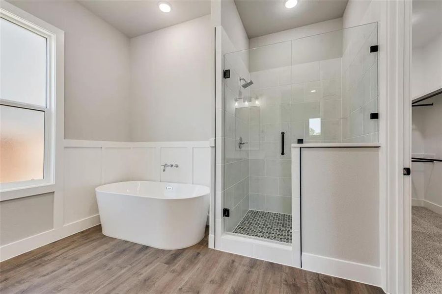 Full bathroom with a freestanding bath, wood finished floors, a stall shower, a wainscoted wall, and a decorative wall