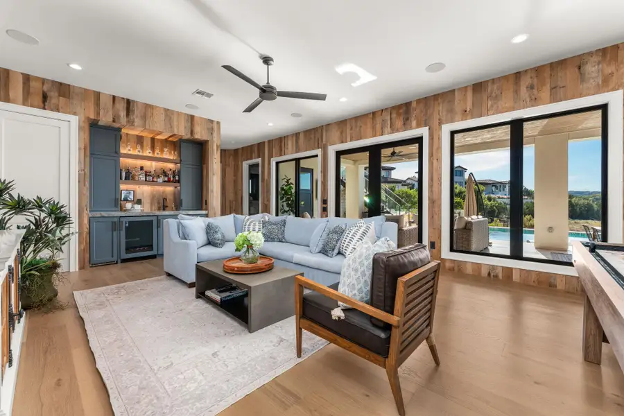 Living room featuring wooden walls, a bar, wine cooler, light wood-style flooring, and a ceiling fan Living room featuring wooden walls, a bar, wine cooler, light wood-style flooring, and a ceiling fan