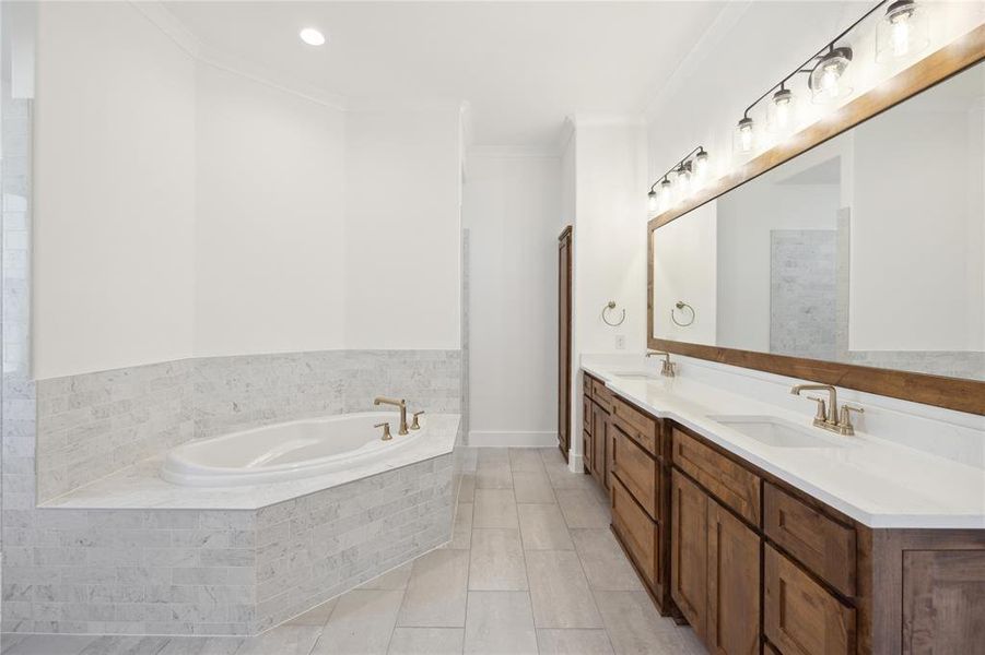 Bathroom with a relaxing tiled tub, dual vanity, tile patterned floors, and ornamental molding