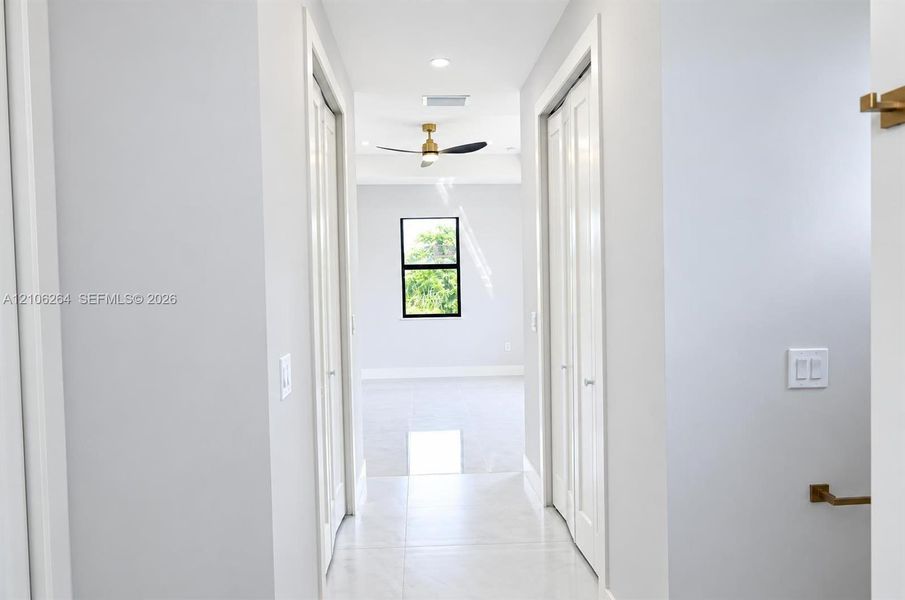 Hallway featuring light-toned tile flooring, recessed lighting, dual bi-fold closet doors, and metallic hardware fixtures