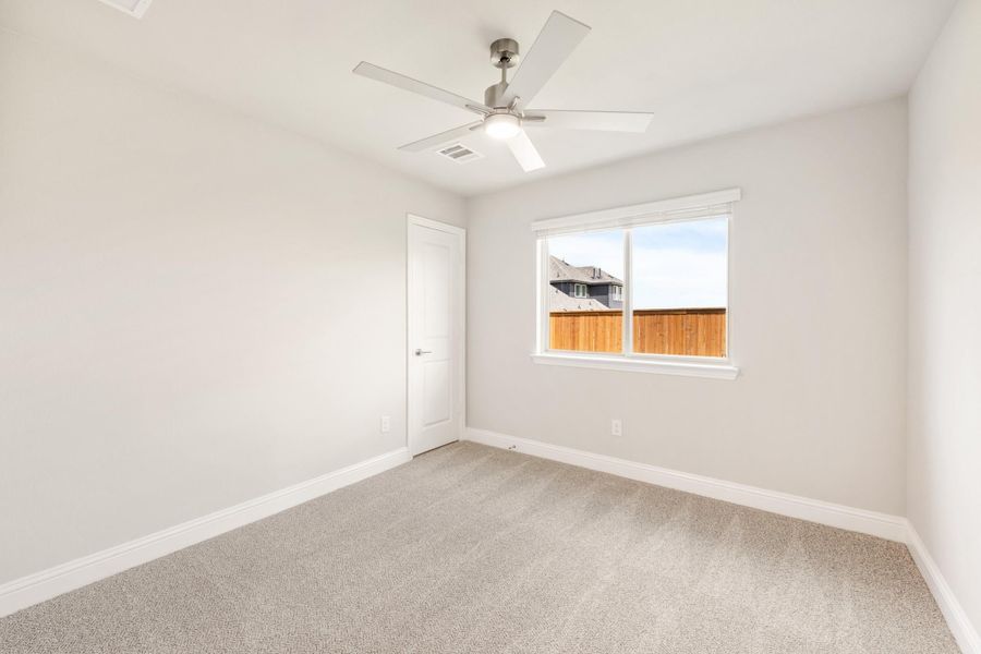 Empty bedroom with gray carpet, ceiling fan, and single window with backyard view