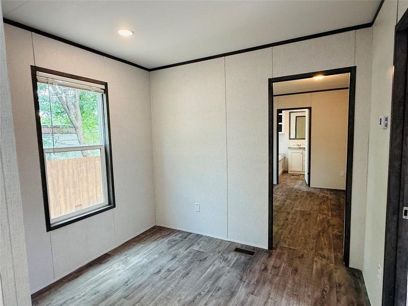 Empty room featuring wood finished floors, crown molding, and visible vents