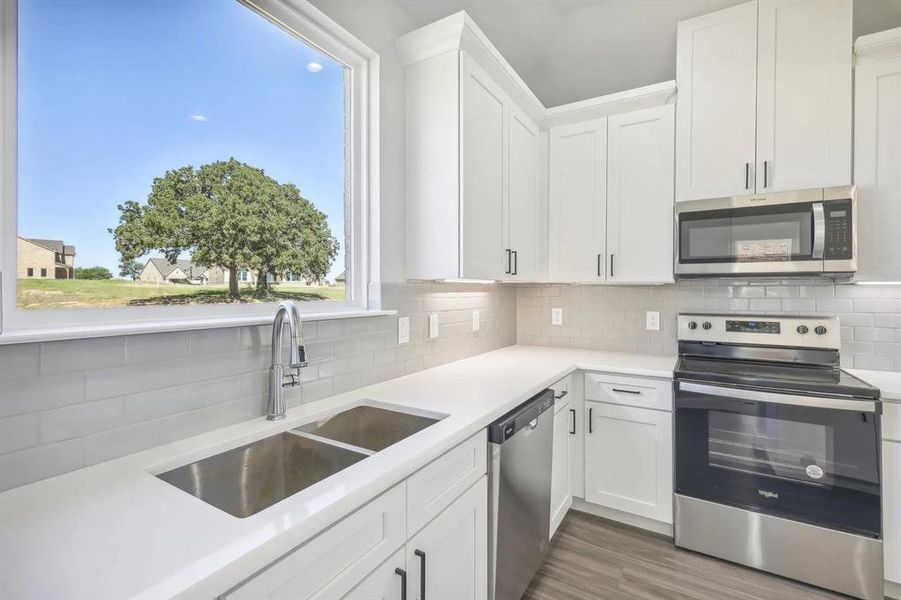 Kitchen featuring appliances with stainless steel finishes, a sink, light countertops, and white cabinetry