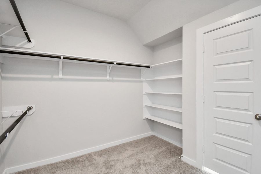 Walk-in closet that epitomizes luxury and practicality. This generously sized space features built-in shelving, offering abundant room for impeccable organization. High ceilings and recessed lighting create a bright and welcoming ambiance. Sample photo of completed home with similar floor plan. Actual colors and selections may vary.