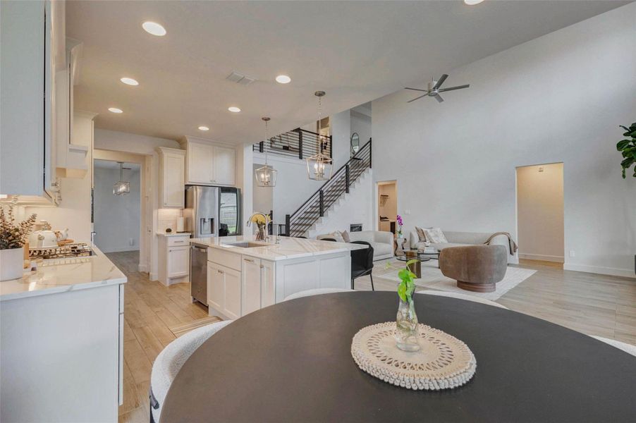 Modern, open-concept living space with high ceilings and abundant natural light. The kitchen features white cabinets, stainless steel appliances, and an island with pendant lighting. The living area includes contemporary furniture and a sleek staircase leading to the upper level. Modern, open-concept living space with high ceilings and abundant natural light. The kitchen features white cabinets, stainless steel appliances, and an island with pendant lighting. The living area includes contemporary furniture and a sleek staircase leading to the upper level.