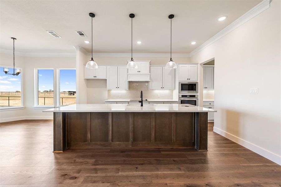 Kitchen with white cabinets, decorative light fixtures, ornamental molding, a large island, and a chandelier