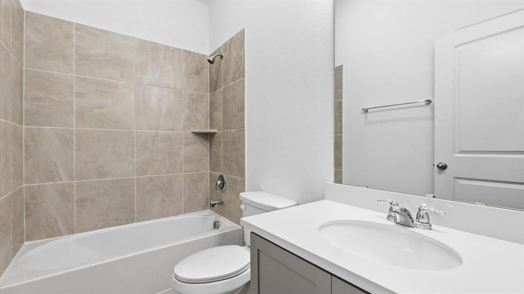 Bathroom featuring a built-in tub with tile surround, a built-in shower niche, a single vanity with an integrated sink, a light-toned countertop, and a mirrored wall