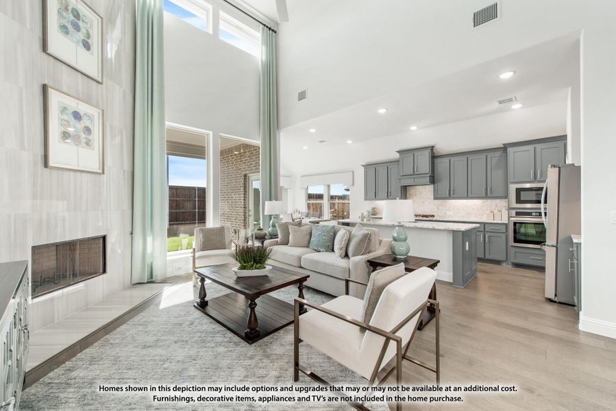 Open-concept living room with two-story ceilings, fireplace, and kitchen with gray cabinets and stainless appliances Open-concept living room with two-story ceilings, fireplace, and kitchen with gray cabinets and stainless appliances