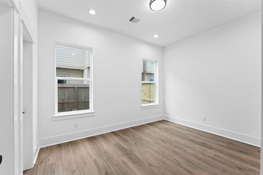 This bright room features large windows for natural light, recessed lighting, white walls, and wood-style flooring, creating a modern and spacious feel.