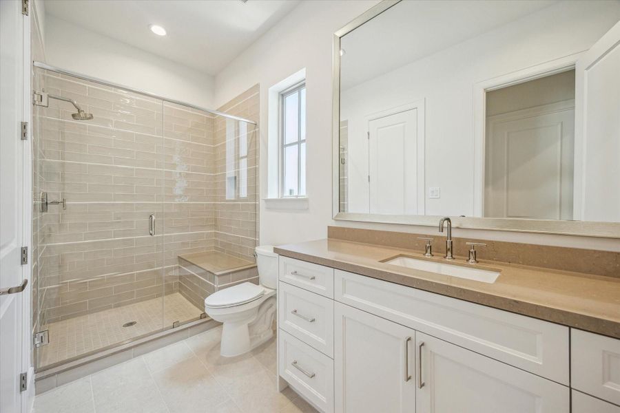 Full bath off secondary features glass enclosed shower with seat and Silestone Coral Clay Quartz countertops.