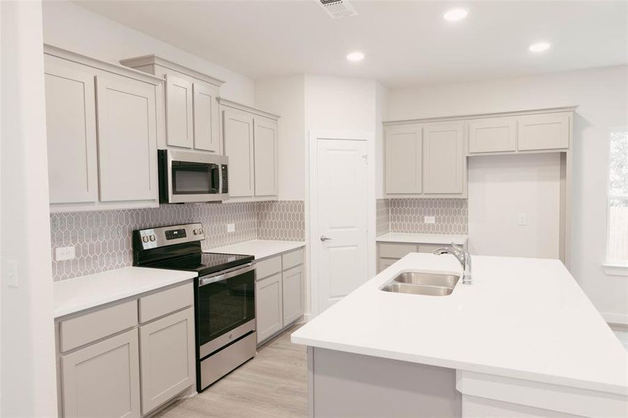 Kitchen featuring appliances with stainless steel finishes, a center island with sink, and backsplash