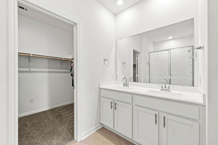 A spacious double vanity connects seamlessly to a large walk-in closet with plush carpeting.