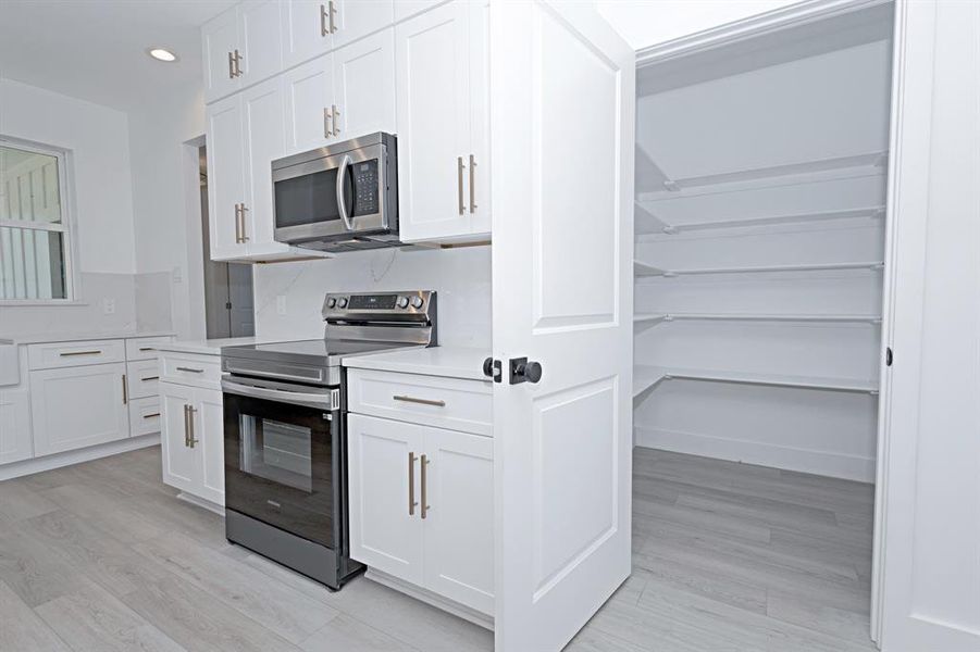 Kitchen with appliances with stainless steel finishes, light countertops, recessed lighting, white cabinetry, and light wood finished floors