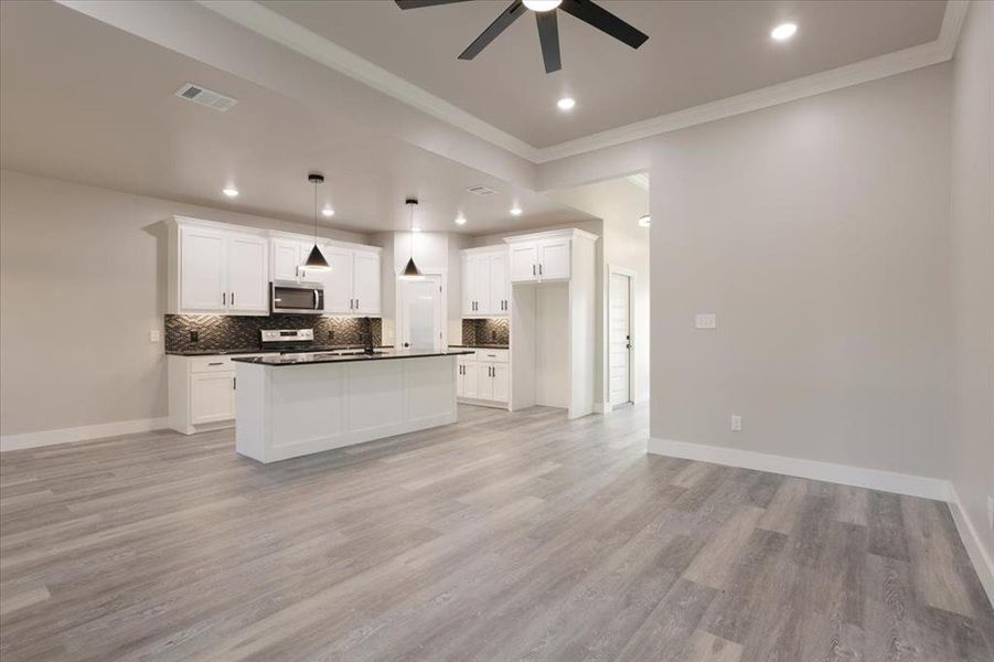 Kitchen with a kitchen island, white cabinetry, pendant lighting, light hardwood / wood-style floors, and stainless steel appliances