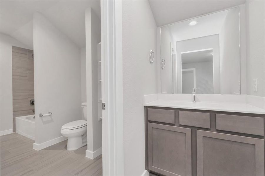 Secondary bathroom, designed for Jack and Jill arrangements, now with a separate vanity area. This well-appointed space showcases stylish tile flooring, a bath/shower combo with an elegant tile surround, and slate colored wood cabinets. Sample photo of completed home with similar floor plan. Actual colors and selections may vary.