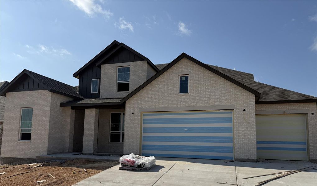 View of front of home with board and batten siding, concrete driveway, brick siding, roof with shingles, and an attached garage