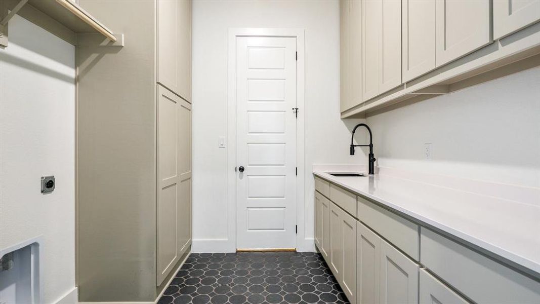 Laundry room featuring sink, hookup for an electric dryer, dark tile floors, and cabinets