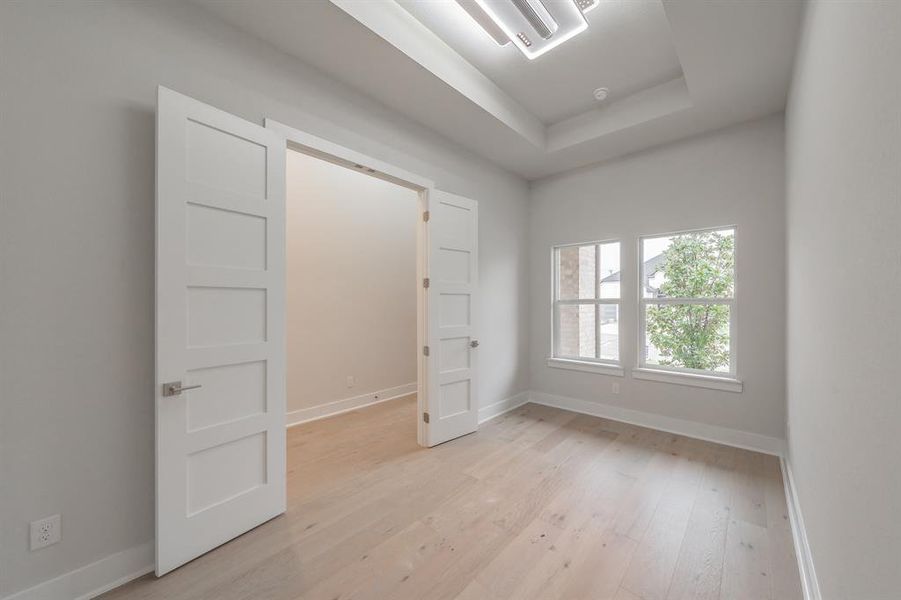 Unfurnished bedroom featuring a raised ceiling and light wood-style flooring