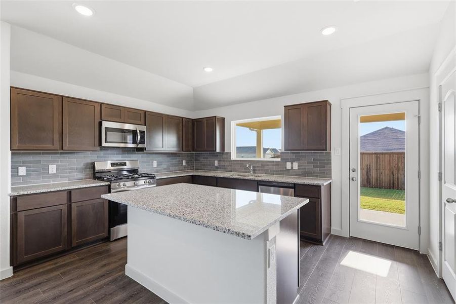 Kitchen featuring dark brown cabinets, stainless steel appliances, light stone counters, a kitchen island, and recessed lighting Kitchen featuring dark brown cabinets, stainless steel appliances, light stone counters, a kitchen island, and recessed lighting