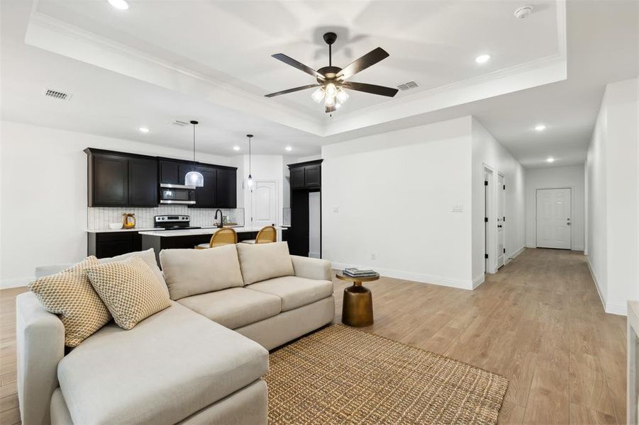 Living room featuring light wood-type flooring, ornamental molding, and a raised ceiling