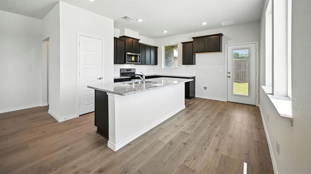 Kitchen with light stone counters, recessed lighting, a center island with sink, dark wood-style floors, and stainless steel appliances