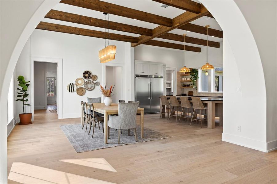 Dining area featuring arched walkways, beam ceiling, and light wood finished floors