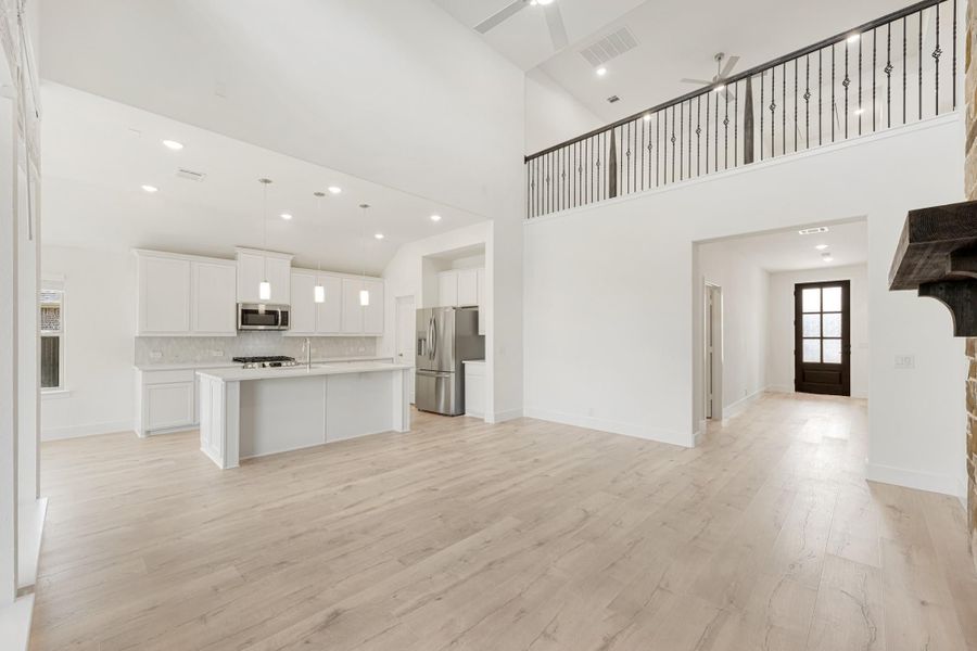Open-concept living area with kitchen island, white cabinets, stainless appliances, high ceilings, and light wood floors