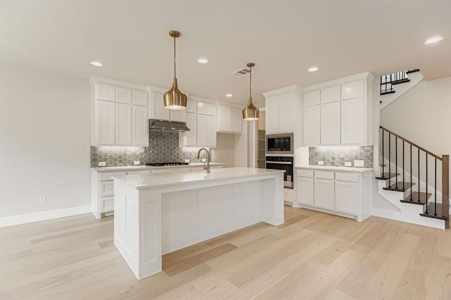 Kitchen featuring oven, stainless steel microwave, under cabinet range hood, decorative backsplash, and light wood-style floors