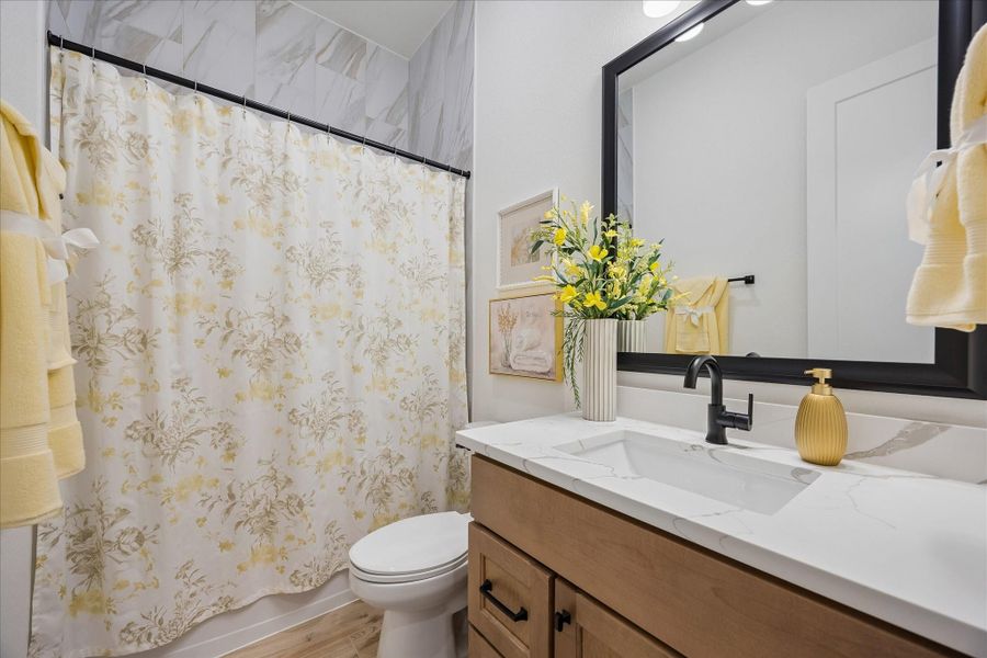 Secondary bathroom features full height upgraded marble tile with matte black upgraded fixtures and framed mirror. Custom cabinetry and granite countertop gives an elevate appearance.