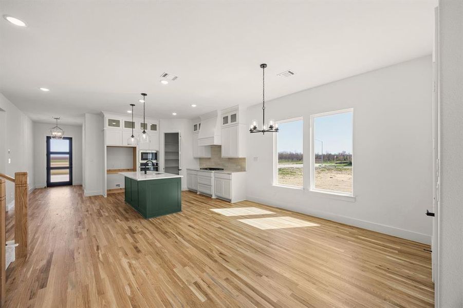 Kitchen featuring a chandelier, open floor plan, a center island with sink, two tone cabinetry, and light wood-style floors
