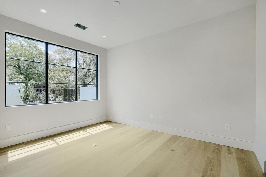 A spacious main level bedroom/office offers ample natural light through a large window overlooking lush greenery.