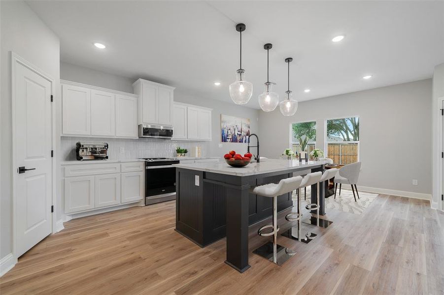 Kitchen featuring light hardwood / wood-style floors, hanging light fixtures, appliances with stainless steel finishes, an island with sink, and tasteful backsplash