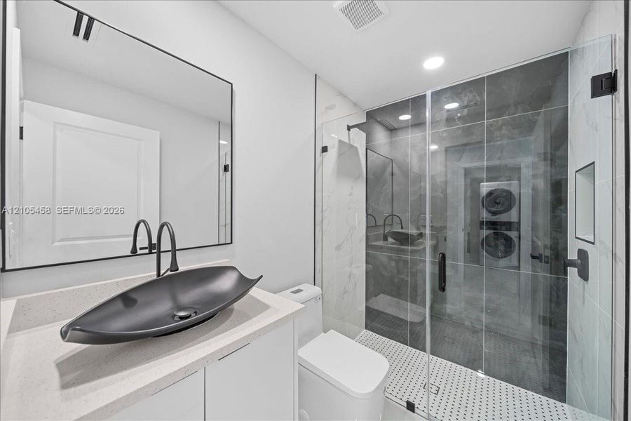 Modern bathroom featuring a glass-enclosed shower, vessel sink with matte black fixtures, white vanity cabinetry, and a light-toned countertop Modern bathroom featuring a glass-enclosed shower, vessel sink with matte black fixtures, white vanity cabinetry, and a light-toned countertop