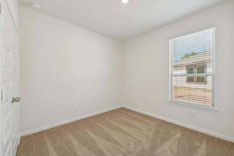 Secondary bedroom features plush carpet flooring, neutral paint, lighting, large window with privacy blinds, and an ample sized closet space.