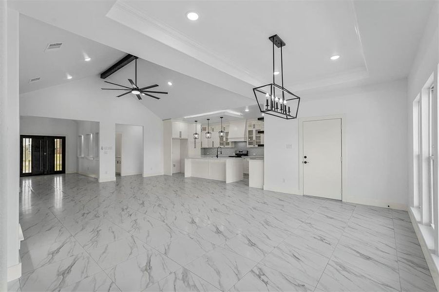 Unfurnished living room featuring ceiling fan with notable chandelier, a wealth of natural light, a tray ceiling, and lofted ceiling with beams