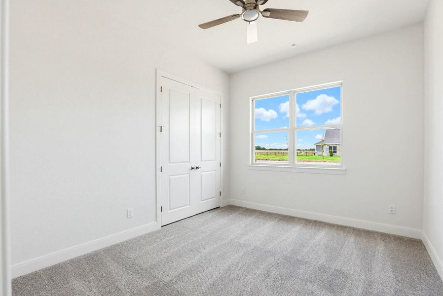 A well-lit bedroom features plush carpeting, a wide window with expansive outdoor views, and a closet with double doors.