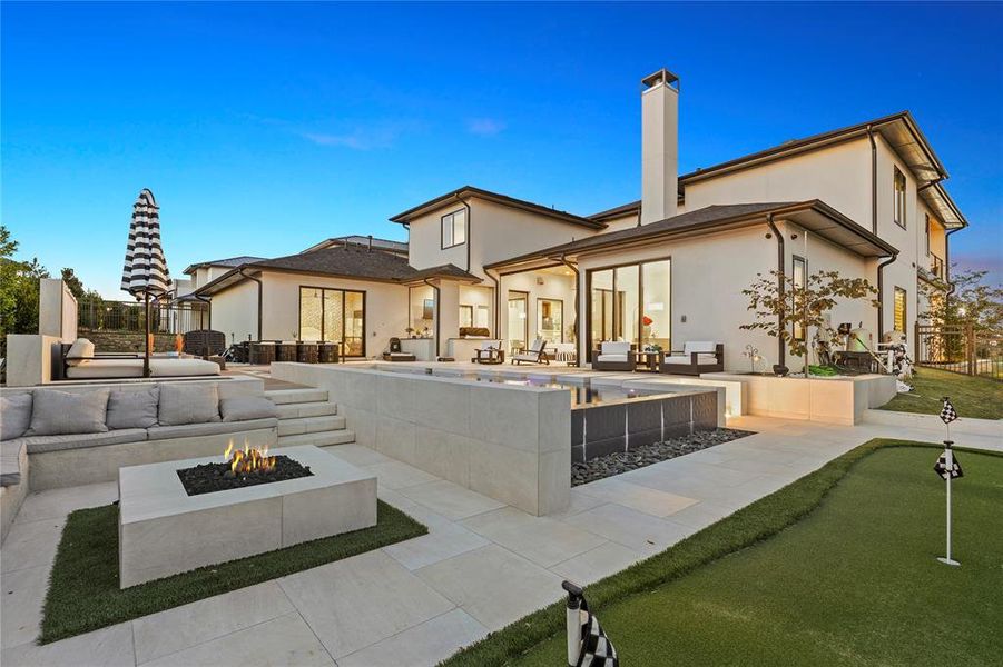 Back of property with an outdoor living space with a fire pit, a putting area, a patio area, a chimney, and stucco siding Back of property with an outdoor living space with a fire pit, a putting area, a patio area, a chimney, and stucco siding