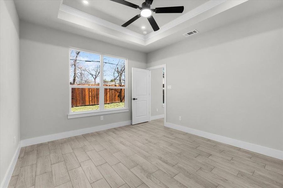 Unfurnished room featuring light wood-style floors, baseboards, visible vents, and a raised ceiling