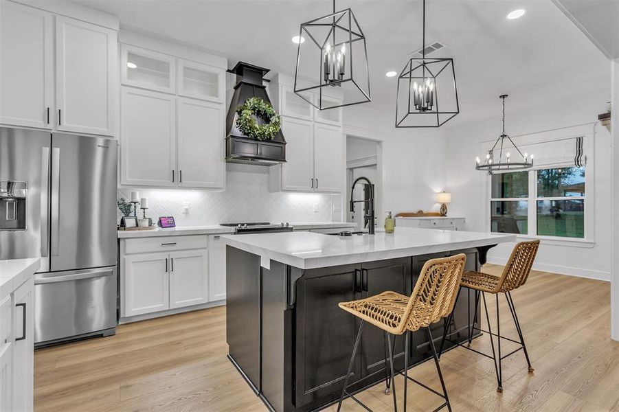 Kitchen featuring stainless steel fridge, a breakfast bar area, hanging light fixtures, white cabinetry, and an island with sink Kitchen featuring stainless steel fridge, a breakfast bar area, hanging light fixtures, white cabinetry, and an island with sink