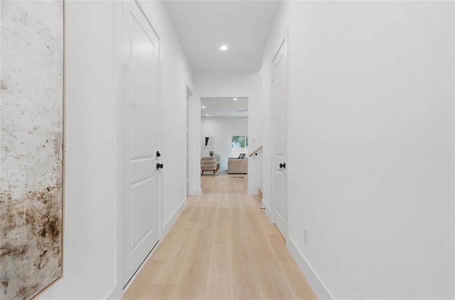Hallway featuring light wood-finish flooring, white walls, recessed lighting, and white paneled doors with matte black hardware Hallway featuring light wood-finish flooring, white walls, recessed lighting, and white paneled doors with matte black hardware